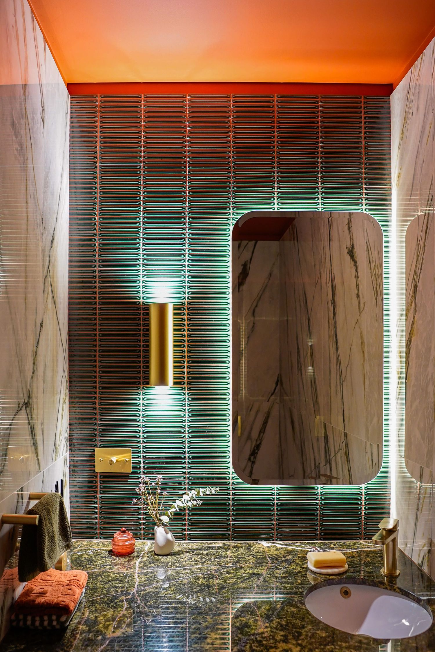 Modern bathroom interior with green tile backsplash, granite countertop, and gold accent lighting casting warm orange glow.