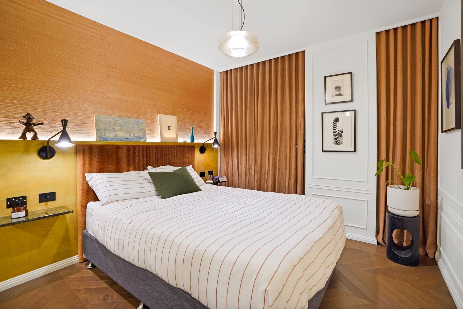 Modern bedroom with wood paneled accent wall, striped bedding, pendant light, and floor-to-ceiling brown curtains.