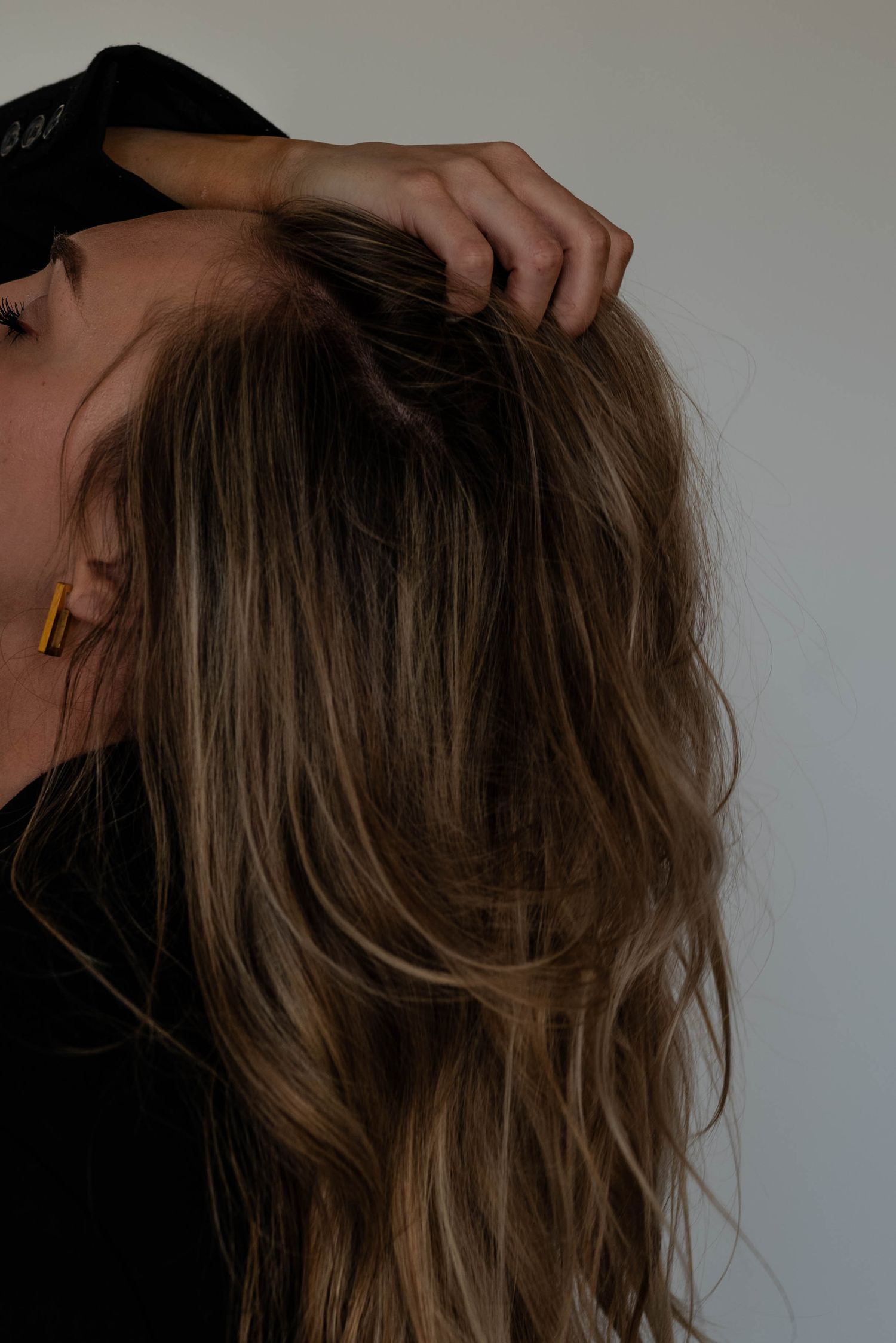 Hand running through highlighted brown hair against neutral background.