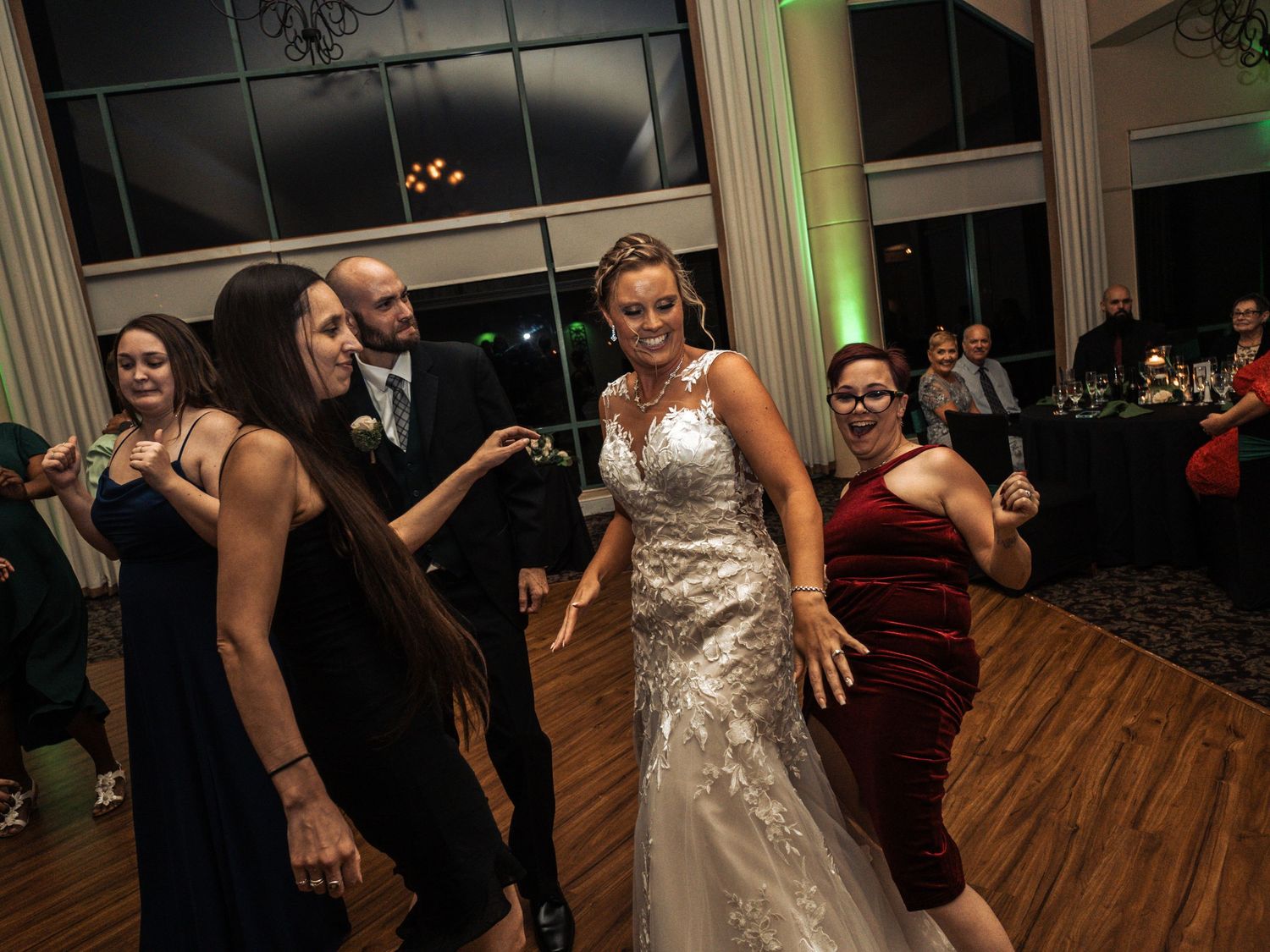 Wedding reception scene with dancing guests on a wooden dance floor under evening lighting.