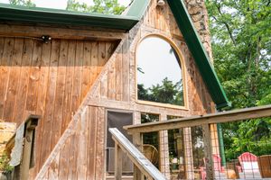 Rustic wooden A-frame cabin exterior with decorative arched window and wooden deck railing.