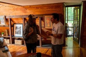 Two people discuss artwork in a rustic wood-paneled gallery space with natural lighting.