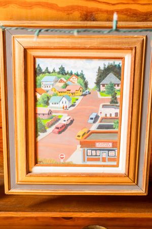 Framed artwork displayed on a wood-paneled wall shows colorful scenes of houses and buildings in a small town.