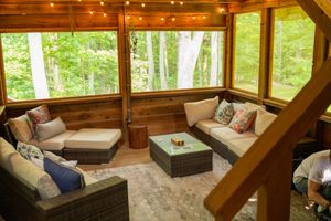 Cozy sunroom with wicker furniture and large windows overlooking lush green forest.