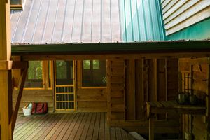 Wooden cabin porch with metal roof and green trim overlooking forest views.