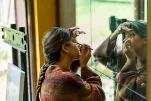 Someone applying makeup while looking in a mirror in a warmly lit room.