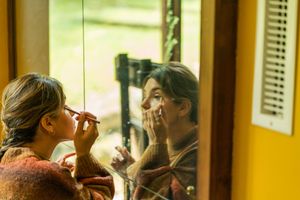 Person applying makeup while looking in a mirror with natural window light.