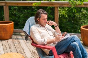 Person relaxing in red outdoor chair on wooden deck surrounded by potted plants.