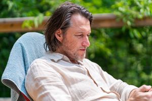 Person resting outdoors in casual attire with a towel draped over chair.