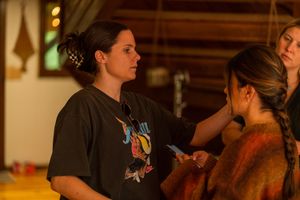 Behind-the-scenes makeup application during film production in warm-lit interior setting.