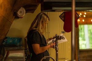 A person operates camera equipment in a dimly lit wooden interior space.