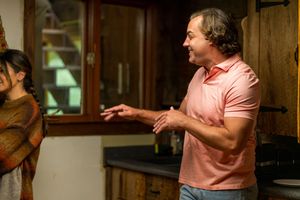 Person in pink polo shirt gesturing while speaking in wooden interior setting.