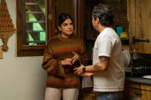Two people engage in conversation while standing in a warmly lit kitchen area.