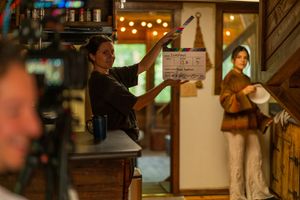 Film crew members work on set with production equipment and ambient lighting.