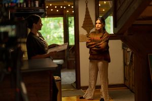 Film crew setting up equipment in rustic interior with string lights and wooden details.