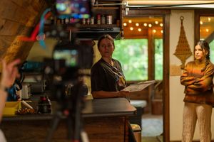 Behind the scenes of film production showing camera operator and crew in rustic setting.