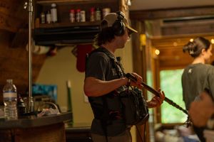 Film crew member with equipment working on production set with warm lighting.