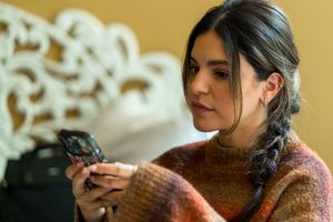 Woman in brown sweater checks her mobile phone while relaxing on couch.