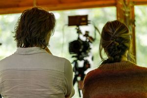 Two people sitting together and looking at camera equipment in a bright room.