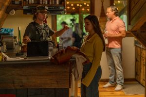 Film crew and staff interact at a rustic bar counter with warm lighting and bar decorations.