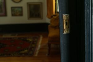 Close-up view of a brass door latch plate mounted on a dark blue door frame with a blurred interior room visible.