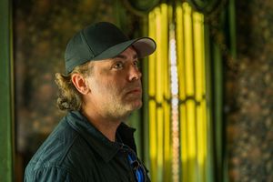Person in baseball cap and dark jacket against decorative wall with yellow lighting.
