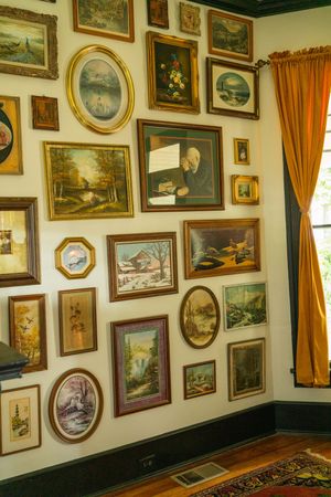 Gallery wall filled with vintage framed paintings and artwork next to yellow curtains in traditional room interior.