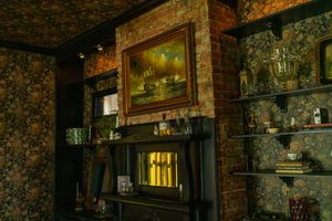 Interior view of vintage room with floral wallpaper, brick fireplace, and framed artwork.