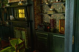 Dark vintage interior with a green chair and black fireplace in a dimly lit Victorian-style room.