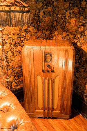 Vintage wooden cabinet with ornate details glows warmly against dark floral wallpaper in retro interior setting.