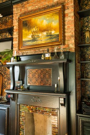 Vintage brick wall interior with ornate gold-framed paintings and dark wood shelving displaying maritime artwork.