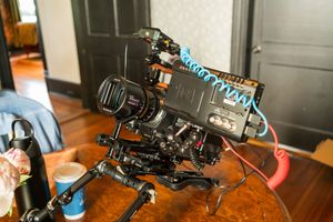 Professional video camera setup with black body and multiple attachments mounted on wooden table surface.