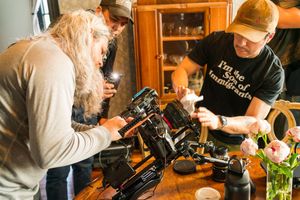 Two camera operators adjust professional filming equipment in a wooden interior.