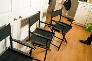 Row of black director chairs lined up on hardwood flooring indoors.