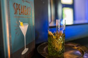 A cocktail menu and martini glass displayed alongside a decorative tiki-style cocktail on a dark bar surface.