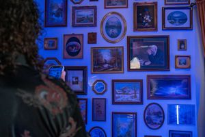 Blue-lit wall covered in vintage picture frames and oval portraits creating a gallery-style display.