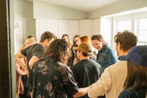 A crowded group of people huddle together in casual attire in a bright white room.