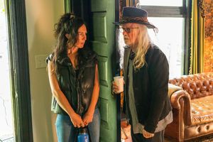 Two women having a conversation in a vintage-style room with a leather couch and green walls.