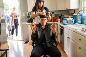 Two people in a bright kitchen performing hair styling activities.