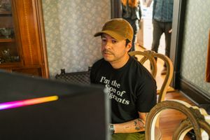 Person wearing a baseball cap and t-shirt works at computer screen in ornate room setting.