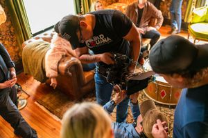 Production crew members huddle around camera equipment on a leather couch in an ornate room.