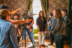 Film director points while giving instructions to crew members and actors on set with professional camera equipment.