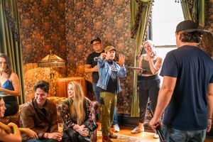 People relaxing and socializing in a vintage-styled room with floral wallpaper and green curtains.