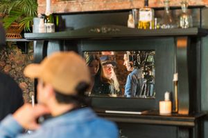 Person reflected in mirror of rustic bar setting with warm lighting and decor.