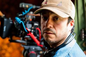 Camera operator wearing a tan baseball cap and denim shirt works with professional filming equipment.