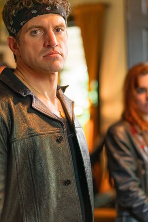 Person wearing a bandana and leather jacket poses confidently in an indoor setting.