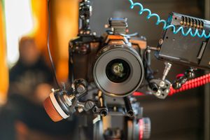 Close-up of a professional camera lens with blue coiled cables and red mounting accessories.