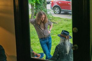 View through doorway of people in casual attire standing outside near a red vehicle.