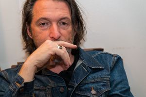Person in denim jacket looking contemplative while resting hand near face.