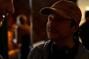 Person wearing baseball cap shown in shadowy lighting against dark background.